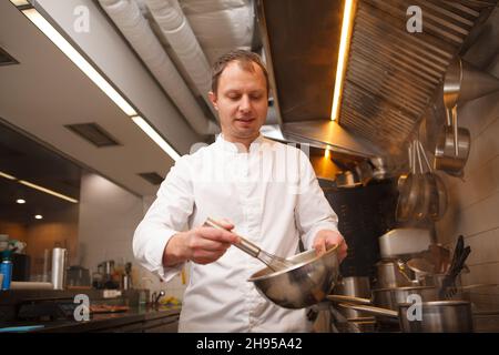 Professional chef smiling, whisking sauce in a bowl, enjoying working at his restaurant Stock Photo