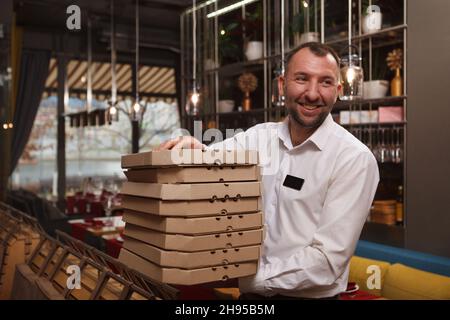 Cheerful waiter smiling, carrying many pizza boxes ready for delivery, copy space Stock Photo