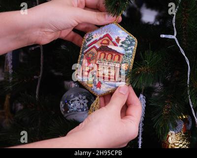 Tambov, Russian Federation - December 02, 2021 A woman hanging a cross stitched ornament on to a christmas tree. This ornament  Noel's Bakery is embro Stock Photo