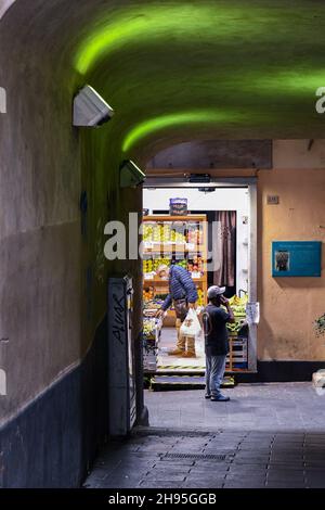A man shopping in a grocery store in a narrow alley (caruggio) in the old town of Genoa at evening, Liguria, Italy Stock Photo