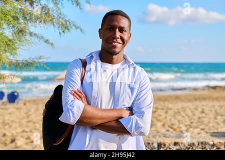 Outdoor portrait of smiling confident man with folded hands, sea nature background. Stock Photo
