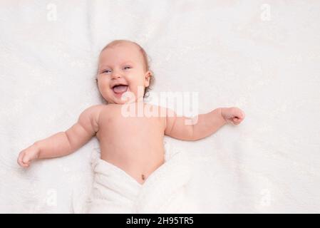 Laughing happy newborn baby girl lies on the bed Stock Photo