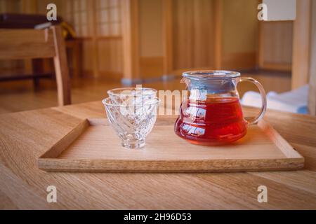 Soft focused elegant glass tea cups and teapot with rooibos herbal tea on traditional japanese wooden kotatsu table in hot springs spa health club Stock Photo