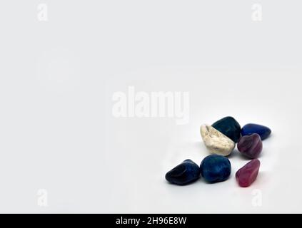 Seven semi-precious gemstones against a white background in the right corner of the photo. They are blue and purple colored. With space to place your Stock Photo