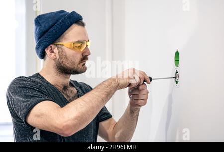 An electrician is mounting electric sockets on the white wall indoors. Stock Photo