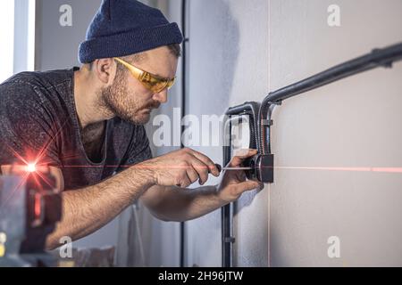 An electrician is mounting electric sockets on the white wall indoors. Stock Photo