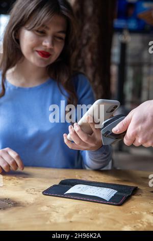 Paypass, male hands holding black pos terminal and female brings smartphone. Stock Photo