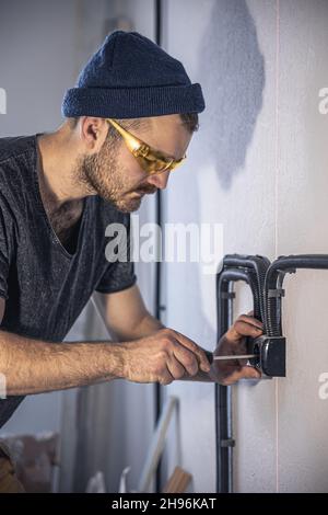 An electrician is mounting electric sockets on the white wall indoors. Stock Photo