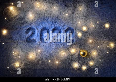 Inscription about the new year 2022 on the snow in winter with christmas lights. Happy New Year greetings concept.