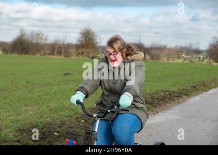 Tienen, Flanders / Belgium - 07 20 2018: Portrait of a young white woman with Down Syndrome driving a tricycle through the fields Stock Photo