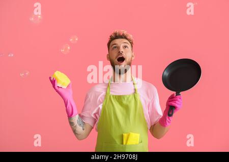 Surprised young man with cleaning sponge and frying pan on pink background Stock Photo