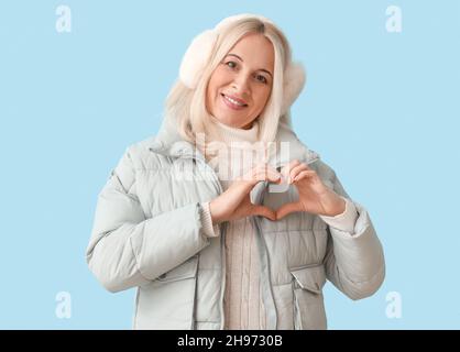 Beautiful mature woman in winter clothes making heart with her hands on color background Stock Photo
