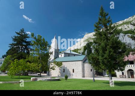 Next to a neat lawn and pretty trees,Serbian style church,made of white stone blocks,pointing towards blue sky in bright sunlight on a summer afternoo