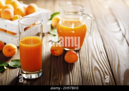 Apricot smoothie in glass on wooden table with crate and jug at background Stock Photo