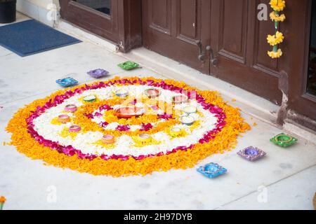 Rangoli pookalam pattern made of flower petals with handmade diya lamps around it on the ground for religious celebrations like diwali, christmas and Stock Photo
