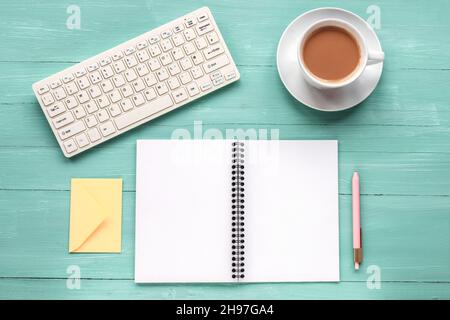 Blank notepad, keyboard, pen and coffee cup on turquoise wooden table. Top view, flat lay, mock up Stock Photo