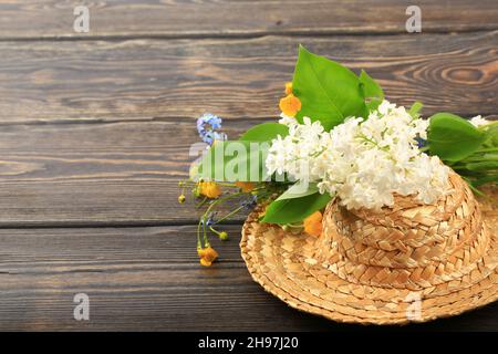 bouquet of spring flowers in a straw hat on a wooden background Stock Photo