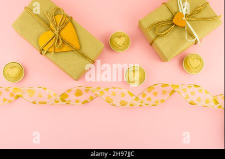 top view of the pink background with festive boxes in craft paper decorated with gold hearts, gold candles in the shape of a heart, silk ribbon Stock Photo
