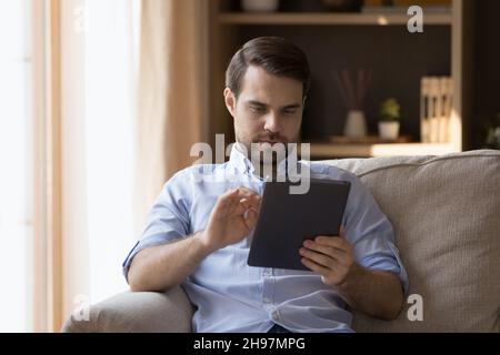 Serious freelance employee man using app on tablet at home Stock Photo