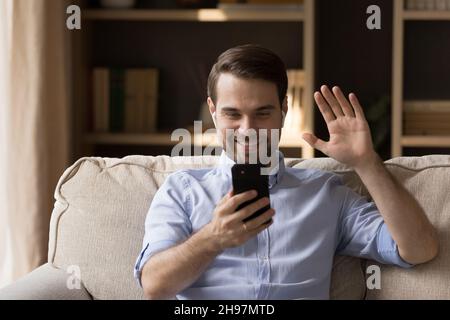 Happy millennial guy with wireless earphones talking on video call Stock Photo