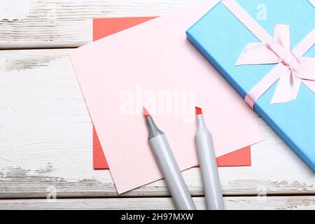 Blue gift box with bow, markers and colored sheets of paper on white wooden background Stock Photo