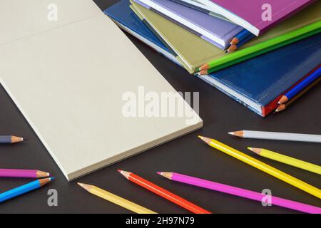 School concept. Colored pencils, colorful  books  and open sketchbook on dark background. Free space for text or picture Stock Photo