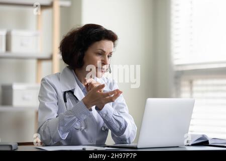 Serious female mid adult doctor using laptop computer at workplace Stock Photo