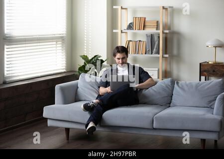 Smiling man in casual using laptop computer on comfortable couch Stock Photo