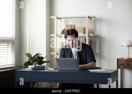 Focused millennial entrepreneur working at laptop at office table Stock Photo