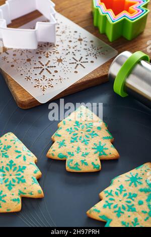 Christmas tree shaped cookies with snowflakes pattern, stencil, cookie cutters, rolling pin, cutting board on a baking mat Stock Photo