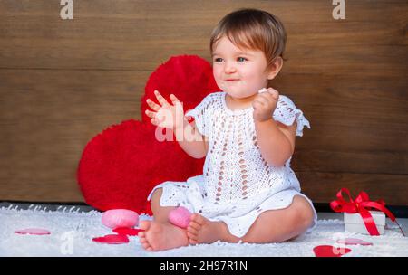 baby with hearts on a wooden background. child in white dress with gifts and hearts Stock Photo