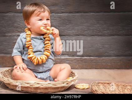 baby with a bagel in the basket on the wooden background. child eats pastries with pleasure Stock Photo