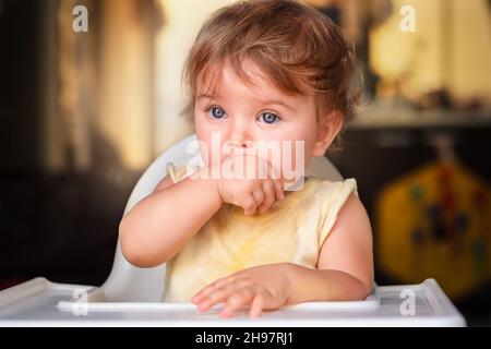 baby sucks hands, first teeth. the child sits in a child seat and looks out the window Stock Photo