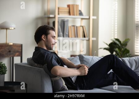 Happy smiling guy working at computer from home couch Stock Photo