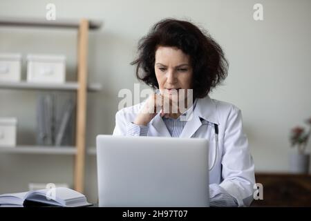 Serious focused senior doctor working at laptop in hospital office Stock Photo