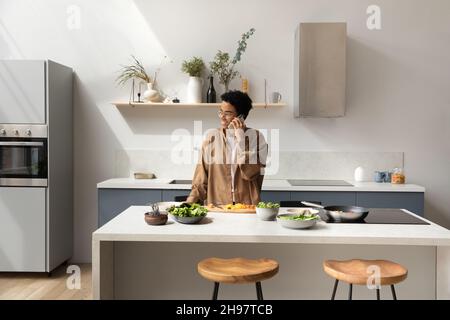Happy young African American woman talking, cooking in kitchen. Stock Photo
