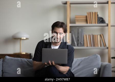 Happy smiling guy working at computer from home couch Stock Photo