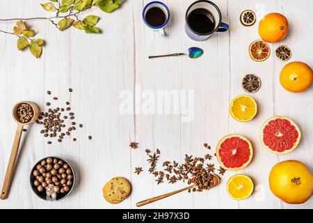 Top view of still life with variety of citrus fruits, chocolate bonbons, paper stars, coffee cups, chocolate cookies and wooden table with star anise Stock Photo