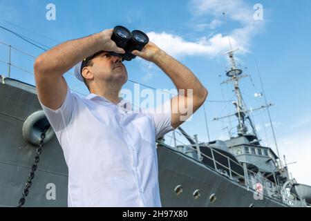 Navy officer standing beside warship and looking around with binocular. Stock Photo