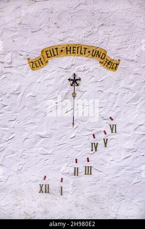Sundial with motto in German ZEIT EILT HEILT UND TEILT (TIME RUNS HEALS AND DIVIDES) on a white house wall. Stock Photo