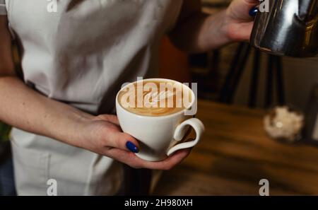Barista prepares cappuccino with latte art. Close-up of the bartender's hands preparing coffee with application to the foam. Stock Photo