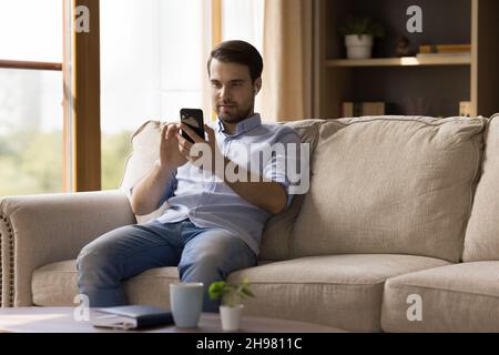 Millennial guy with earphones using media app on mobile phone Stock Photo