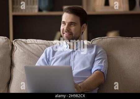 Happy thoughtful young man working at laptop from home Stock Photo