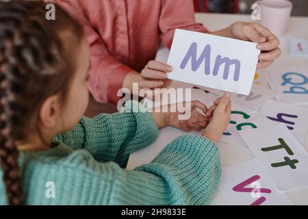 Close-up of teacher showing the card with letter to little girl while they learning English at the table Stock Photo