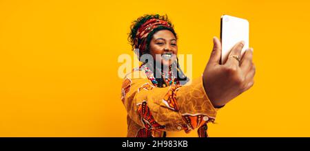 Creating bright memories. Fashionable young woman taking a selfie while wearing traditional African clothing. Happy young woman smiling cheerfully whi Stock Photo