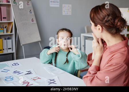 Little schoolgirl learning to read English words together with the teacher while they studying at desk in the classroom Stock Photo