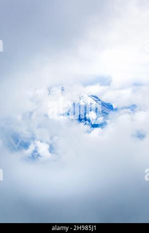 The top of a mountain appears through the thick clouds in the mountains. Stock Photo