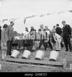 Copthall Stadium, Hendon, Barnet, London, 25/06/1966. A man throwing a ball in a game of Ball in the Bucket at a funfair held during the annual Laing Sports Day at Copthall Stadium In 1966, the annual Laing employees' Sports Day was held on 25th June at Copthall Stadium in Hendon. It was the first time the event had been held there, having previously taken place the Laing Sports Ground at Elstree. A range of events included athletics and a football competition, and competitors travelled from the firm's regional offices and sites, including from Scotland and Carlisle. There was also a funfair, Stock Photo