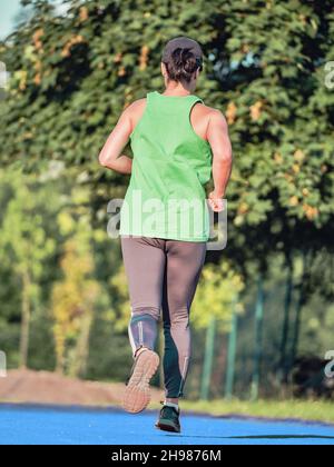 Mature woman in green singlet and gray leggings runs. Keep