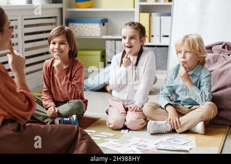 A group of children sitting on the floor and repeating new words after the teacher during an English lesson at school Stock Photo